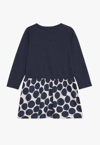 Šaty s dlouhým rukávem, modrý top a bílá sukně s velkými modrými puntíky; příjemný materiál a nařasený detail v pase u dolního okraje.
