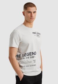 Camiseta blanca de algodón con texto gráfico negro y coordenadas en el frente. Cuello redondo clásico y mangas cortas. Ajuste casual.