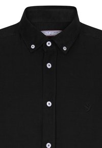 Sort fløjlsskjorte med knap-ned krave, hvide knapper og et broderet fuglelogo på venstre bryst. Struktureret stof.