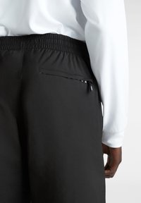 Schwarze Sporthosen mit einem elastischen Bund, ausgestattet mit einer Rückentasche mit Reißverschluss und einem glatten, leichten Stoff.