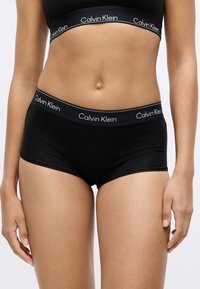 Fekete pamut boxer alsónadrág egyszínű kivitelben, széles elasztikus derékpánttal, amelyen fehér betűkkel a "Calvin Klein" felirat olvasható.