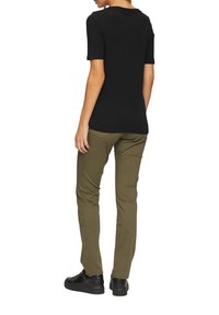 Zwarte korte mouwen t-shirt gecombineerd met olijfgroene broek en zwarte sneakers met dikke zool. Gladde stof, slim-fit ontwerp en subtiele stikdetails.