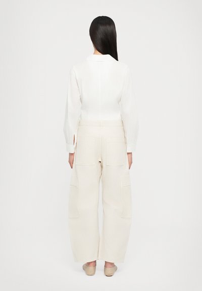 Witte blouse met lange mouwen en een kraag, gecombineerd met beige cargobroek met meerdere zakken en een ruime fit. Gladde stoftextuur.