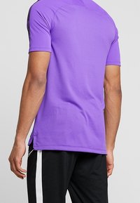 Purple short-sleeve athletic shirt with textured fabric, featuring side slits and contrasting black accents on the shoulders.