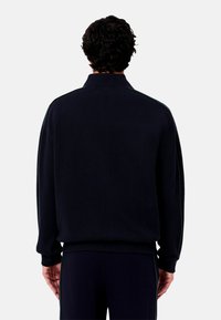 Marineblaues Sweatshirt mit hohem Kragen und grünen Seitenstreifen. Hergestellt aus strukturiertem Stoff, mit gerippten Bündchen und Saum.