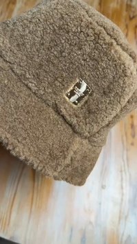 Brown wool hat with a soft, textured surface. Features a small metallic brand tag on the side, showcasing a square shape and polished finish.