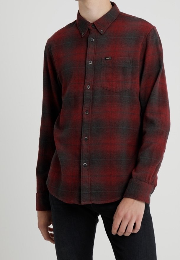 Camicia di flanella a quadri rossa e nera con colletto a punta, taschino frontale e maniche lunghe. Texture morbida con cuciture e bottoni visibili.
