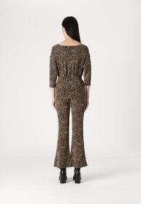 Combinaison rayée marron et noire avec des manches trois-quarts, un pantalon évasé et une taille ajustée, fabriquée à partir d'un tissu texturé. Chaussures noires chunky.