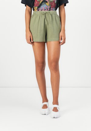 Shorts verts avec une ceinture élastique et un cordon de serrage, présentant une coupe décontractée et une texture légère, associés à des chaussures blanches.