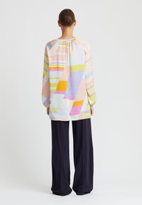 Langärmlige Bluse aus leichtem Stoff mit einem mehrfarbigen abstrakten Muster, mit gerafftem Ausschnitt und lockerer Passform. Kombiniert mit dunklen Hosen.