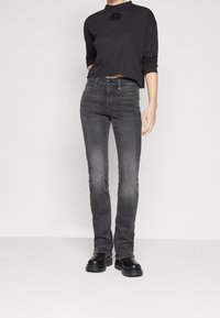 Sudadera negra recortada con un logo bordado y mangas largas, combinada con jeans ajustados grises y botas de plataforma negras.