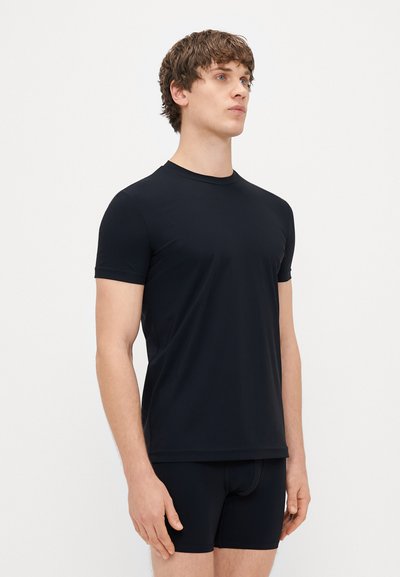 T-shirt nera a maniche corte realizzata in tessuto liscio e leggero. Presenta una scollatura a girocollo e un design semplice e aderente. Indossata con pantaloni neri.