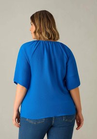 Blusa blu texturizzata con maniche a lunghezza del gomito, scollo rotondo e vestibilità rilassata, abbinata a jeans in denim aderenti.