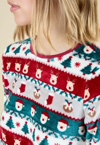 Fleece trui met een rood en groen kerstpatroon met rendieren, kerstman gezichten, bomen en sokken op een witte achtergrond.