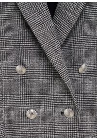 Blazer croisé à carreaux gris et noirs avec quatre boutons décoratifs métalliques et larges revers crantés.