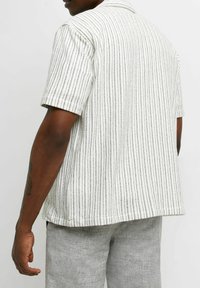 Lyhythihainen valkoinen kauluspaita mustilla pystysuorilla raidoilla, teksturoidusta kankaasta ja väljällä istuvuudella. Näkyvissä takakuvasta.