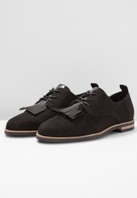 Chaussures en daim noir à semelles plates, dotées d'un design à lacets, d'accents décoratifs à franges et de talons noirs brillants.