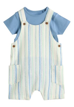 Chemise bleue à manches courtes sous une salopette courte à rayures blanches, bleues et vertes avec poches avant et boutons en bois sur les bretelles.