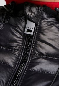 Svart puffjacka med en glänsande finish, horisontell sömnad, framzipper med DKNY-logotyp och justerbar dragsko i kragen.