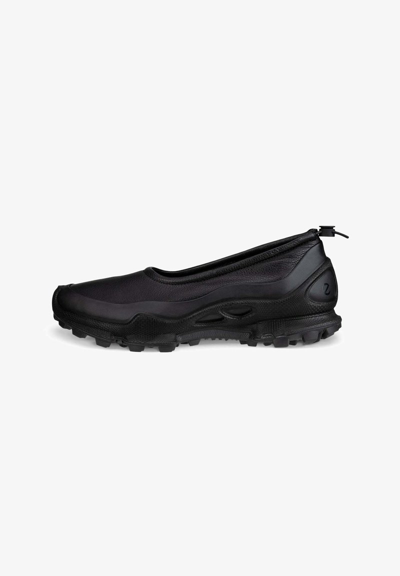 Chaussure noire à enfiler avec semelle texturée, bout arrondi et bouton réglable au talon, conçue pour une utilisation en extérieur ou décontractée.