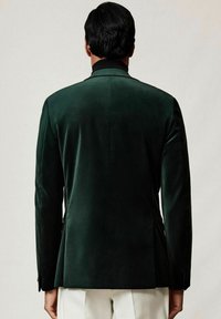 Tumedate roheline sametist bleiser, millel on kohandatud lõige, soonikuga kaelus ja üks ventilatsioon. Õlgadel ja varrukatel on liistude detailid.