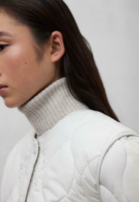 Witte gewatteerde bomberjack met een hoge, geribbelde beige coltrui. Gladde textuur met subtiele stiksels langs de naden.
