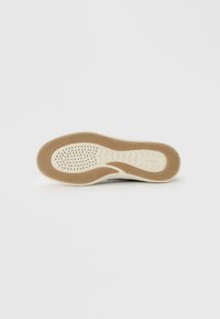 Shoe outsole featuring a light rubber base with a textured brown pattern, white midsole with ventilation holes, and overall curved shape.