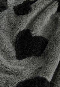 Harmaa fleecepeite, jossa koholla olevat mustat sydänkuviot, pehmeä, teksturoitu pinta ja hillitty kiilto.