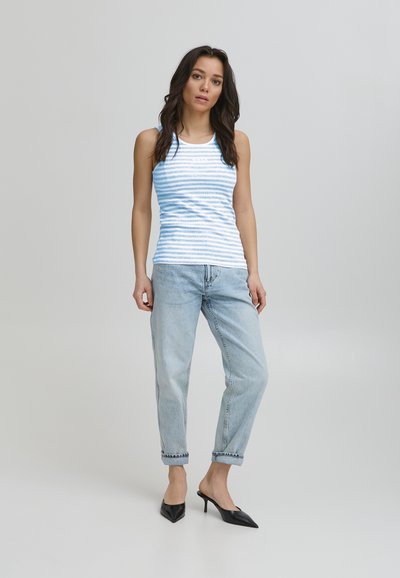 Ribade sinine top, sobitava kujuga, koos heledate madala vöökohtadega teksade ja mustade terava ninaga kontsakingadega. Sile kangastekstuur.