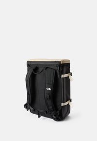 Svart ryggsäck med en beige topp; har vadderade axelremmar, en strukturerad design och sidodetaljer. Tillverkad av hållbara material för utomhusbruk.