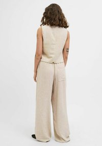 Heledbeez š sleeveless topp ja laiad püksid vertikaalsete triipudega. Kanga tekstuur on käe läbi näha; sisaldab selja nupudetaili ja taskut.