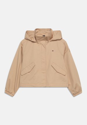 Beige cropped jack met capuchon, twee voorzakken, elastische manchetten en een klein logo op de linkerkant van de borst. Gemaakt van zachte, gladde stof.