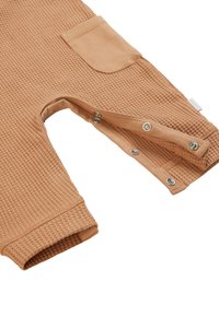 Combinaison en tissu gaufré, de couleur brun clair, avec des manches longues, dotée d'une poche à rabat et de pressions en bas pour un habillage facile.