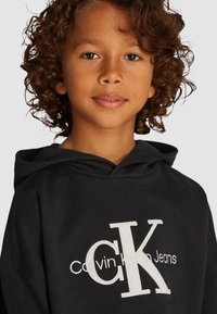 Felpa nera con tasca a marsupio frontale e logo "CK" ricamato bianco. Tessuto morbido, con design della cappuccio regolabile.