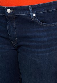 Jeans de mezclilla azul oscuro con una textura suave, que cuentan con una bragueta de botones, bolsillos laterales y sutiles acentos de costura.