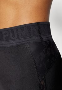 Sorte leggings med en struktureret sort talje i livet med 'PUMA' logo. Stoffet er glat med et subtilt mønster på siderne.