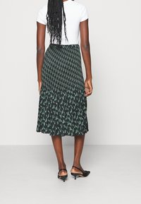 Sukně s černým a zeleným vzorem, sklady s rozšířeným tvarem, nošená s bílým topem a černými lodičkami, ukazující hladkou texturu látky.