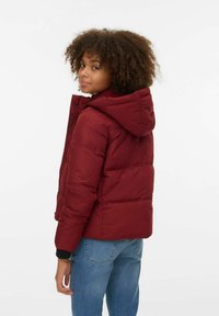 Burgunderfarget dunjakke med hette, quiltet design og ribbestrikkede mansjetter. Kombinert med lyseblå jeans for en avslappet stil.