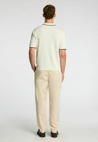 Polo shirt a maglia in bianco sporco con dettagli neri, abbinato a pantaloni beige. Design semplice e dal taglio rilassato con maniche corte e scollatura rotonda.