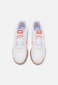 Weiße Sportschuhe mit einer glatten Oberseite, die pinke Akzente und eine strukturierte Gummisohle aufweisen. Schnürdesign mit Branding auf der Zunge.