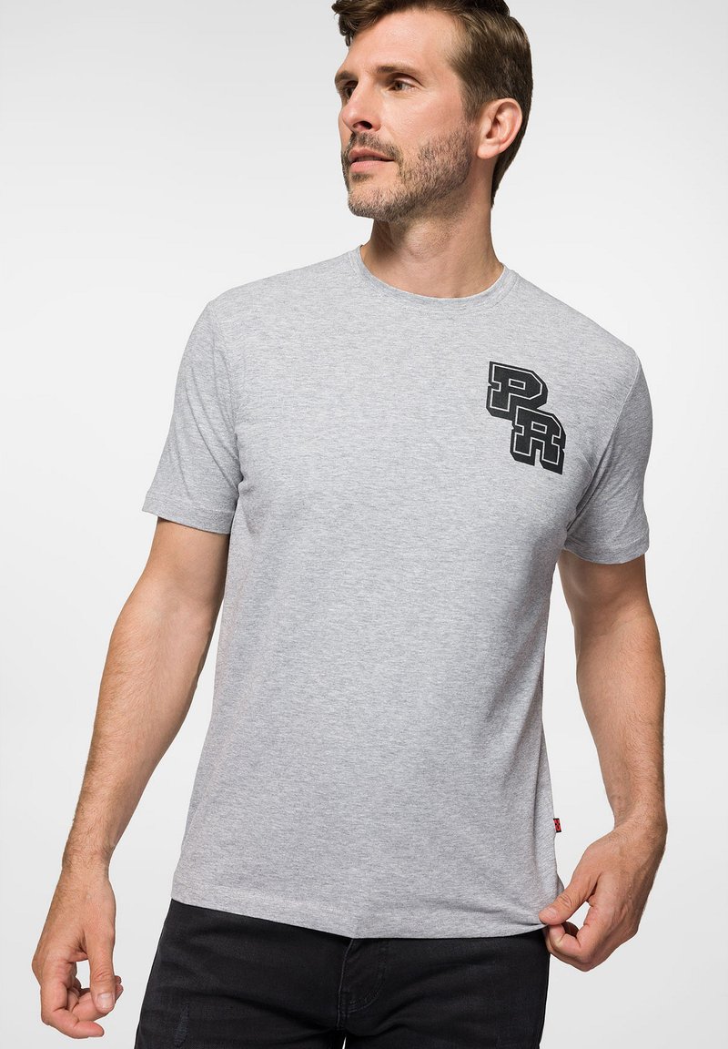 Szara koszulka wykonana z miękkiej bawełny, z krótkimi rękawami, okrągłym dekoltem i wyraźnym czarnym logo "PR" po lewej stronie klatki piersiowej.