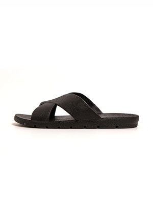 Black slide sandal featuring crisscross straps made of textured material, flat sole with subtle tread pattern, and minimalist design.