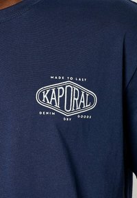 T-shirt en coton bleu marine présentant un logo graphique blanc avec l'inscription "KAPORAL MADE TO LAST" et les mots "DENIM DRY GOODS" en dessous.