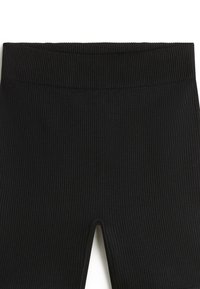 Svarta räfflade leggings med en bred midjeband, som har en utskärning vid fållen. Tyget har en mjuk, texturerad yta.