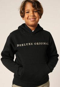 Zwart capuchontrui met de opdruk "DEELUXE ORIGINAL" in goud. Voorzien van een kangoeroezak en geribbelde boorden. Zachte stofstructuur.