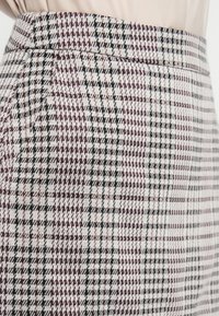 Rutet nederdel i nuancer af burgunder, sort og hvid; har en tætsiddende talje og struktureret stof med et subtilt houndstooth-mønster.
