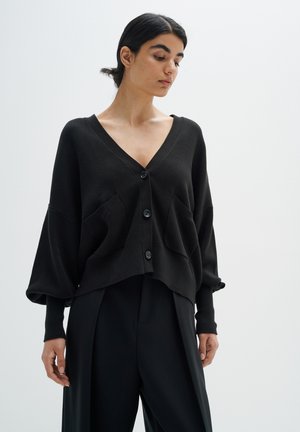 Zwarte, cropped cardigan van een zachte gebreide stof met een V-hals, grote knopen en zijzakken. Heeft lange, losse mouwen met manchetten accenten.