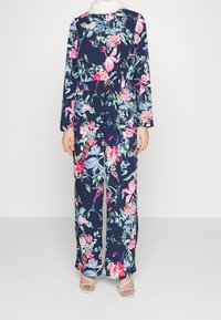 Kombinezon w kwiatowy wzór z głębokim granatowym tłem oraz żywymi różowymi, niebieskimi i zielonymi kwiatami. Długie rękawy i szerokie nogawki.