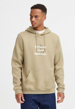 Sudadera color beige con un bolsillo frontal, que presenta un estampado gráfico que dice "EXPANDE TU MENTALIDAD" en colores contrastantes y cordones.