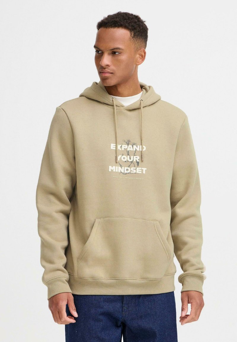 Sudadera color beige con un bolsillo frontal, que presenta un estampado gráfico que dice "EXPANDE TU MENTALIDAD" en colores contrastantes y cordones.
